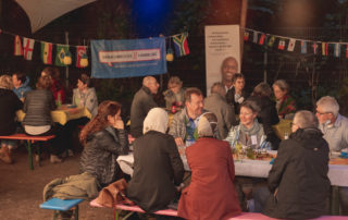 Mehrere Personen sitzen zusammen auf einer Bierbank, wahrscheinlich bei einem gemeinsamen Fest