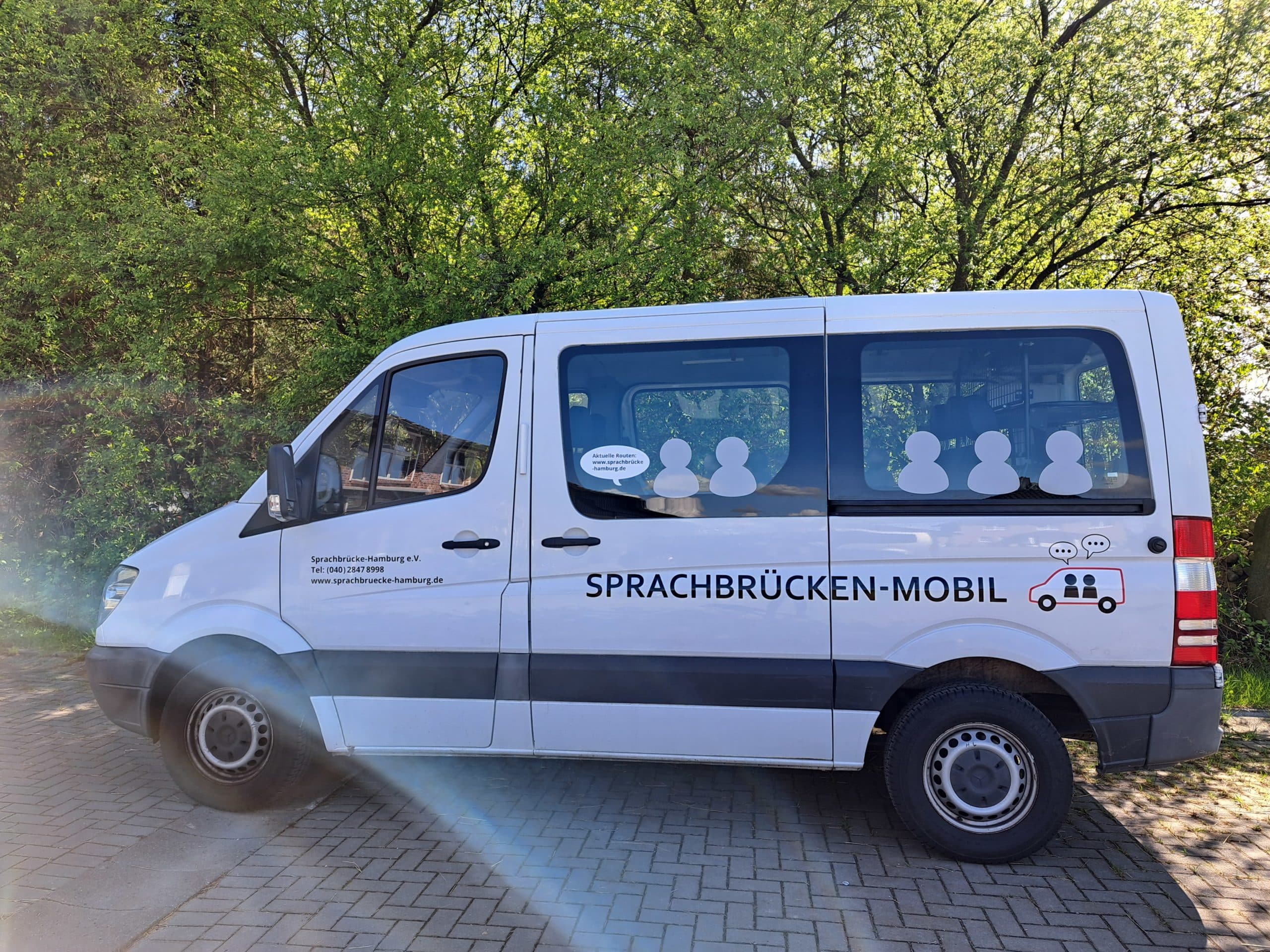 Weißer Sprinter in der Seitenansicht zu sehen. Auf der Seite steht Sprachbrücken-Mobil sowie die Adresse von Sprachbrücke-Hamburg e.v.